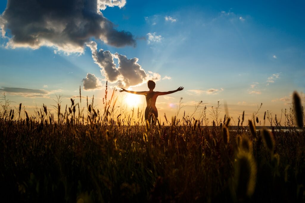 Silhouette of sportive girl practicing yoga in field at sunrise.
